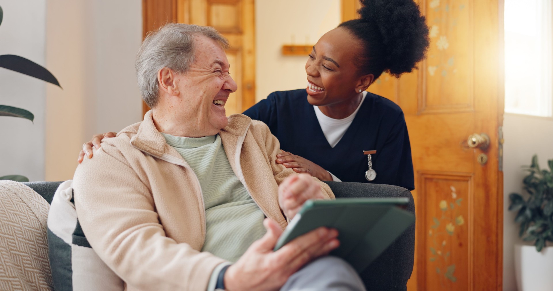 Tablet, nurse and senior man on sofa browsing on internet for medical consultation research. Bonding, healthcare and black woman caregiver talking to elderly patient networking on technology at home.